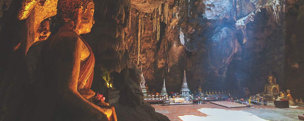 a view into Tham Khao Luang Cave showing a large buddha statues and various other relics